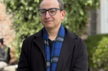 Retrato de académico Sergio Galdames con gafas, chaqueta negra y bufanda colorida en exteriores.