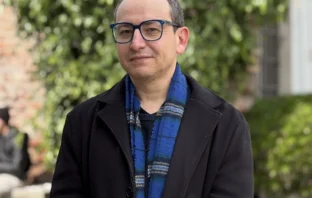 Retrato de académico Sergio Galdames con gafas, chaqueta negra y bufanda colorida en exteriores.
