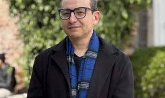 Retrato de académico Sergio Galdames con gafas, chaqueta negra y bufanda colorida en exteriores.